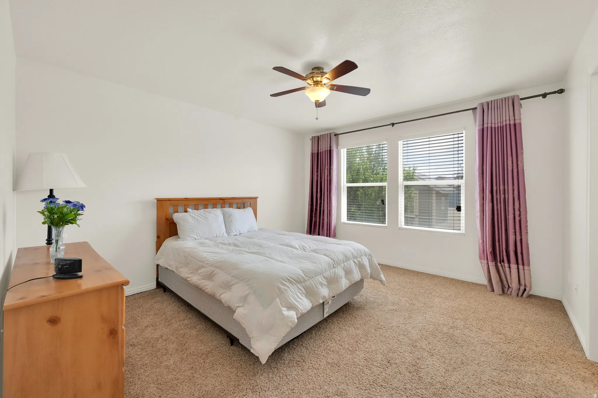 Bedroom featuring textured carpet flooring, a ceiling fan with integrated lighting, and two large windows equipped with blinds