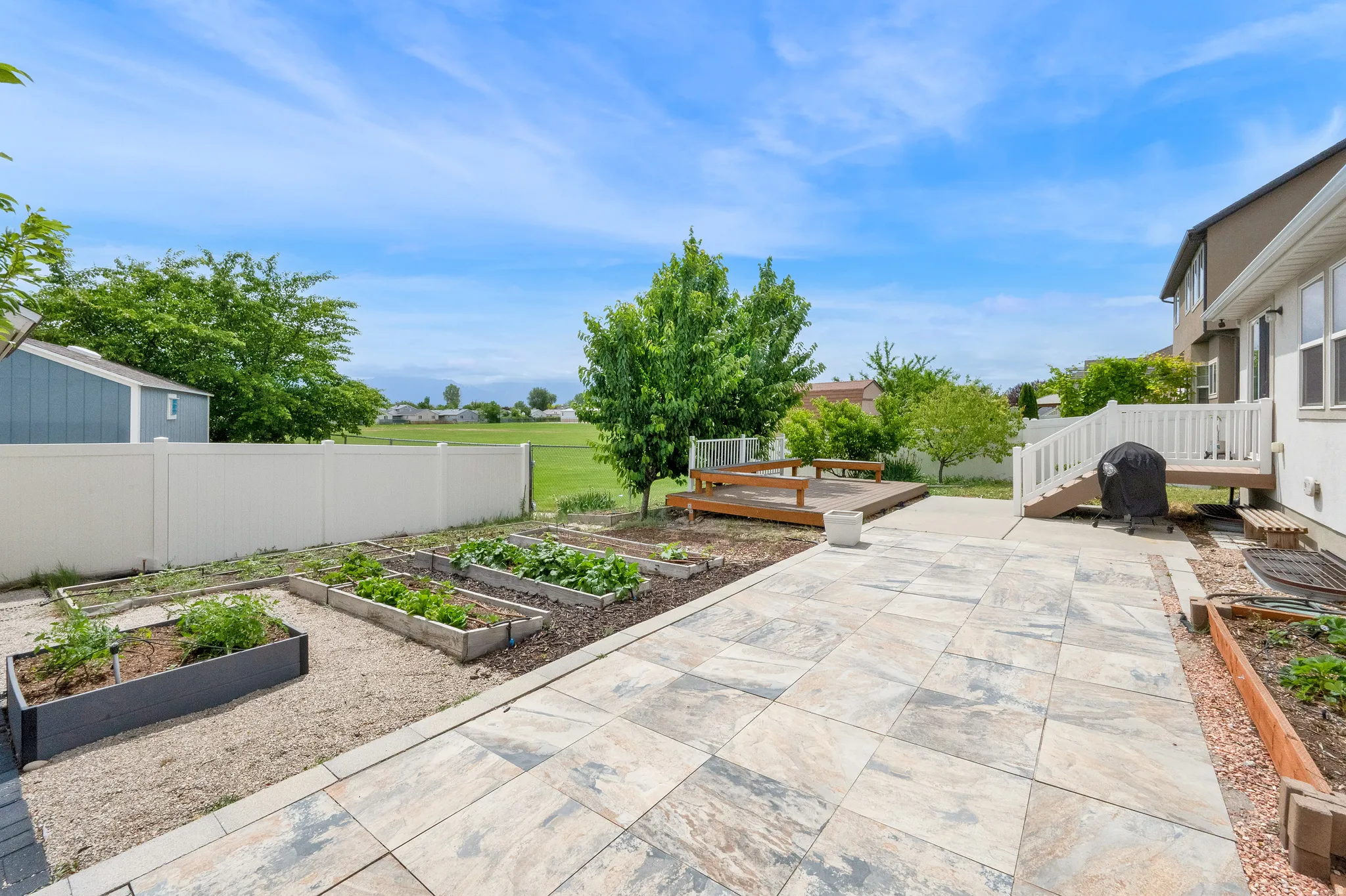 Expansive backyard featuring a large paver patio, a raised wood deck, and multiple raised garden beds