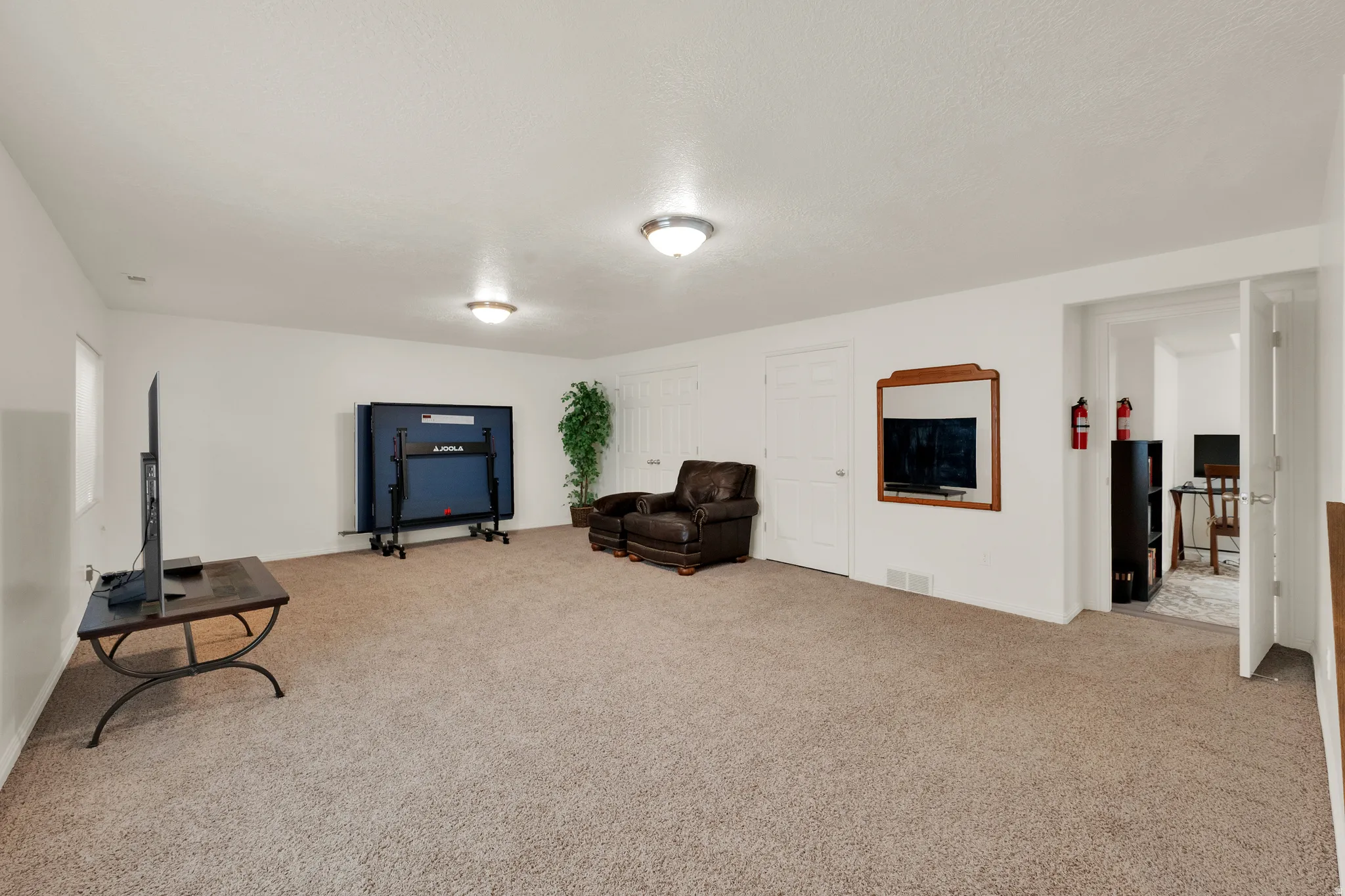 Expansive carpeted room featuring white walls and ceiling, flush-mount lighting, and an additional room entry