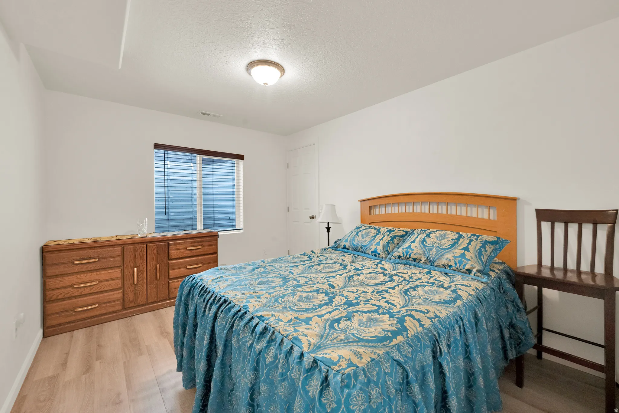 Bright interior room featuring wood-finish flooring, a window with horizontal blinds, a ceiling-mounted light fixture, and white painted walls