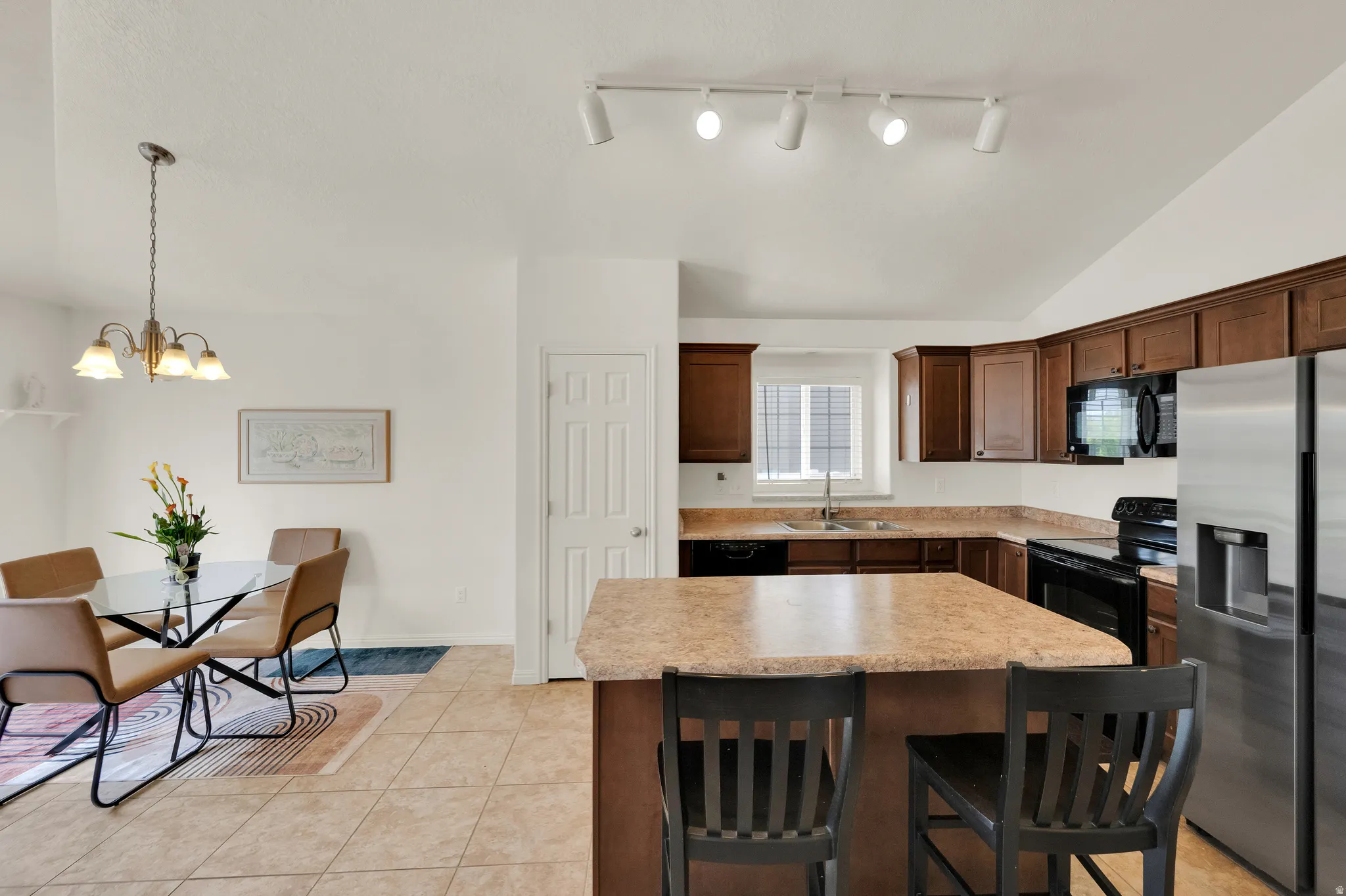Kitchen featuring wood-finish cabinetry, stainless steel refrigerator, black electric range, and a central island with bar seating