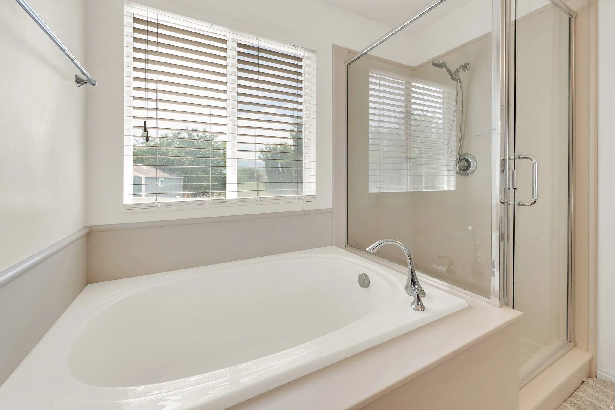 Corner soaking tub with chrome fixtures, adjacent to a glass-enclosed shower with a multi-function showerhead
