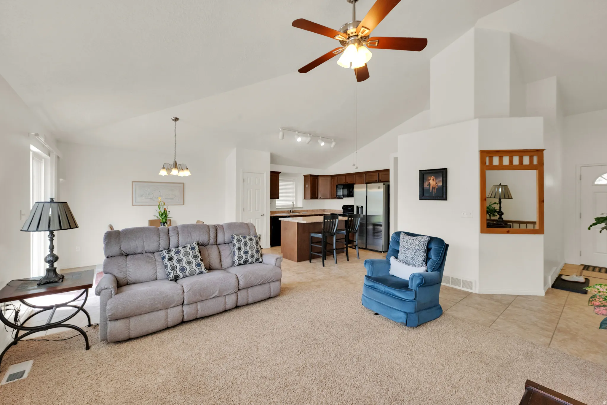 Spacious living area featuring vaulted ceilings, a ceiling fan, and carpet flooring