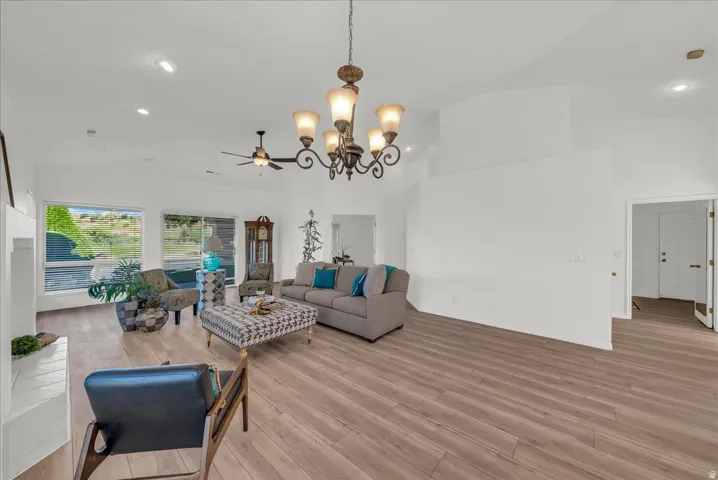 Spacious living area featuring vaulted ceilings, wood-finish flooring, recessed lighting, a ceiling fan, and large windows offering abundant natural light
