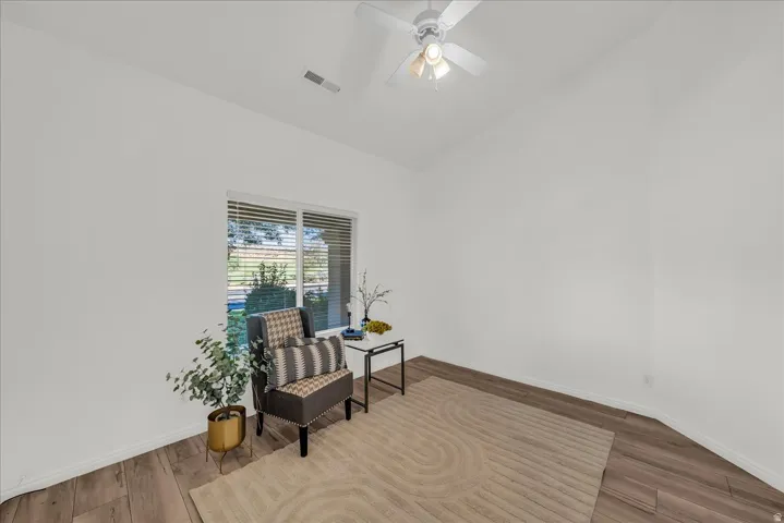 Room featuring wood-finish flooring, a white ceiling fan with integrated lighting, and a large window with blinds