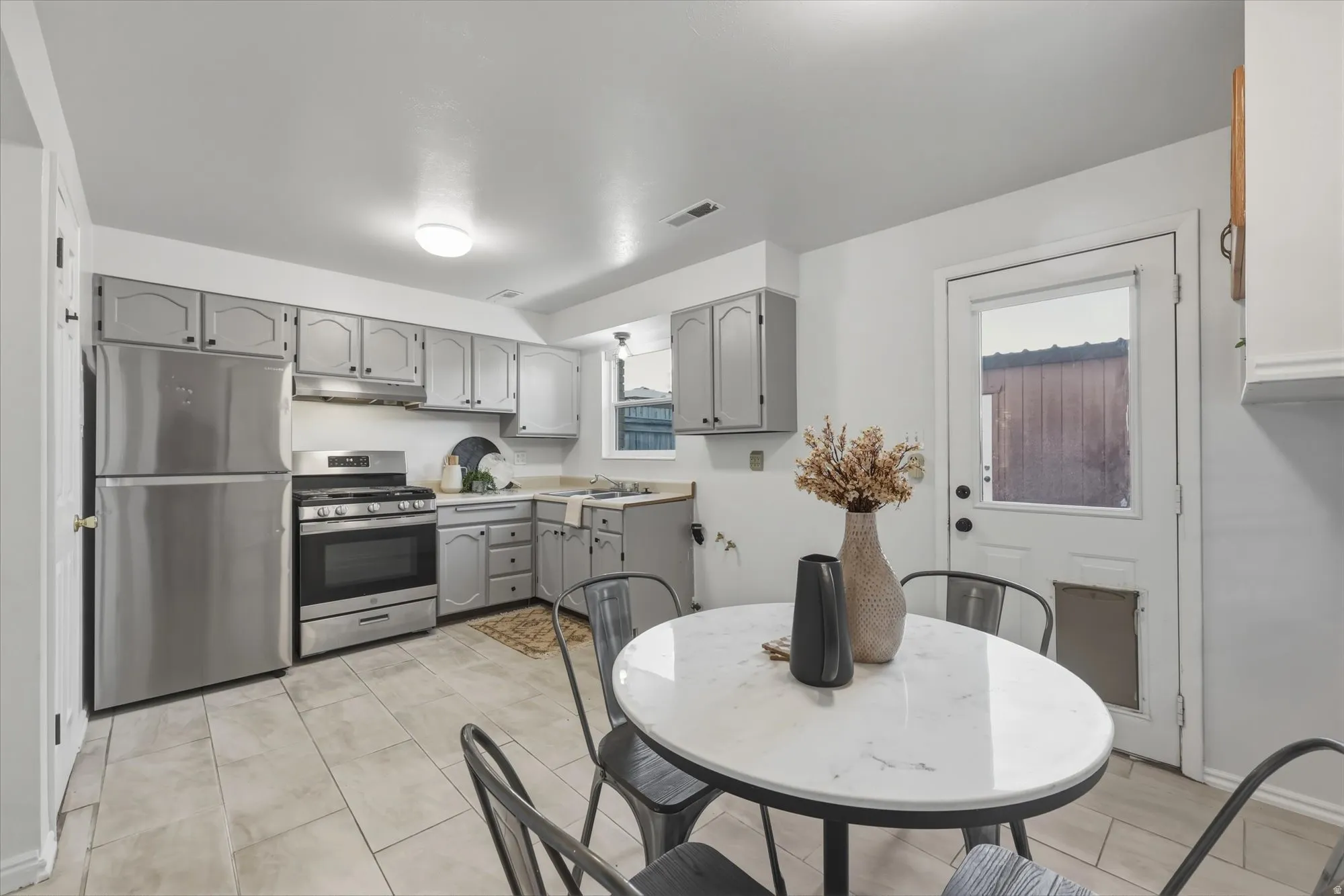 Kitchen with gray cabinetry, stainless steel appliances, and light-toned tile flooring