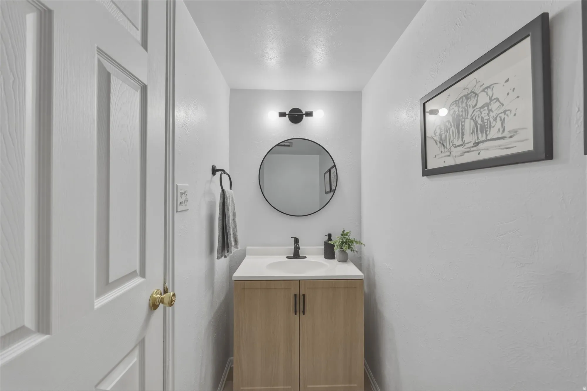 Compact bathroom featuring a light wood-finish vanity with dual cabinet doors, a white countertop, and a circular undermount sink