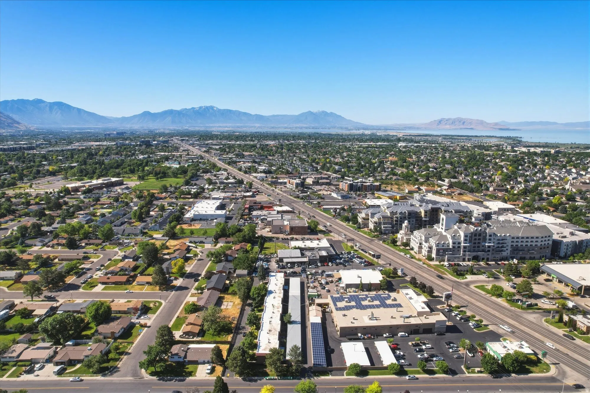 Aerial perspective showcasing a broad urban landscape with varied architectural styles, a prominent multi-lane thoroughfare, and extensive green spaces
