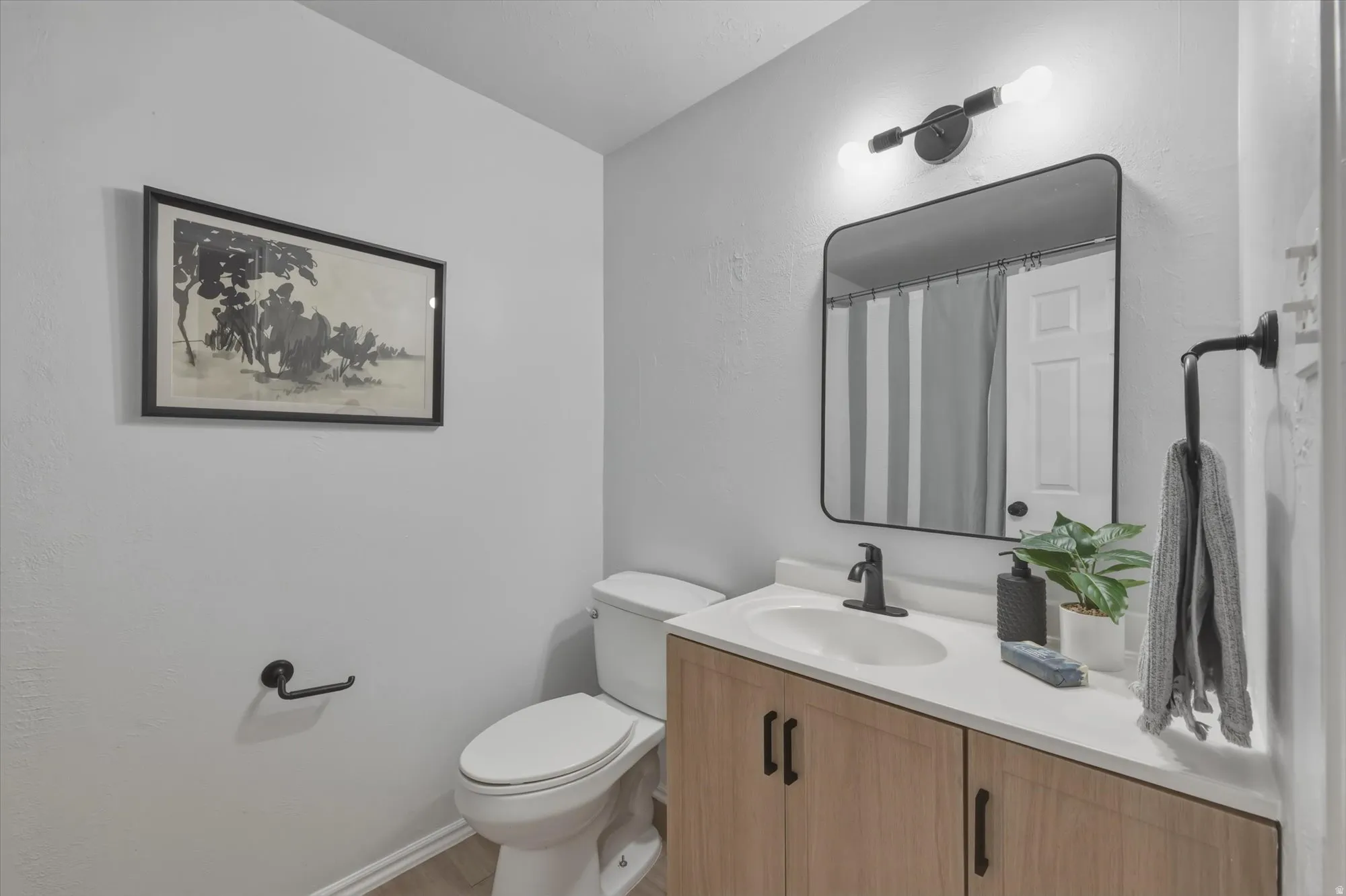 Bathroom featuring a light wood-finish vanity with a white countertop and integrated sink, matte black faucet, and a contemporary framed mirror