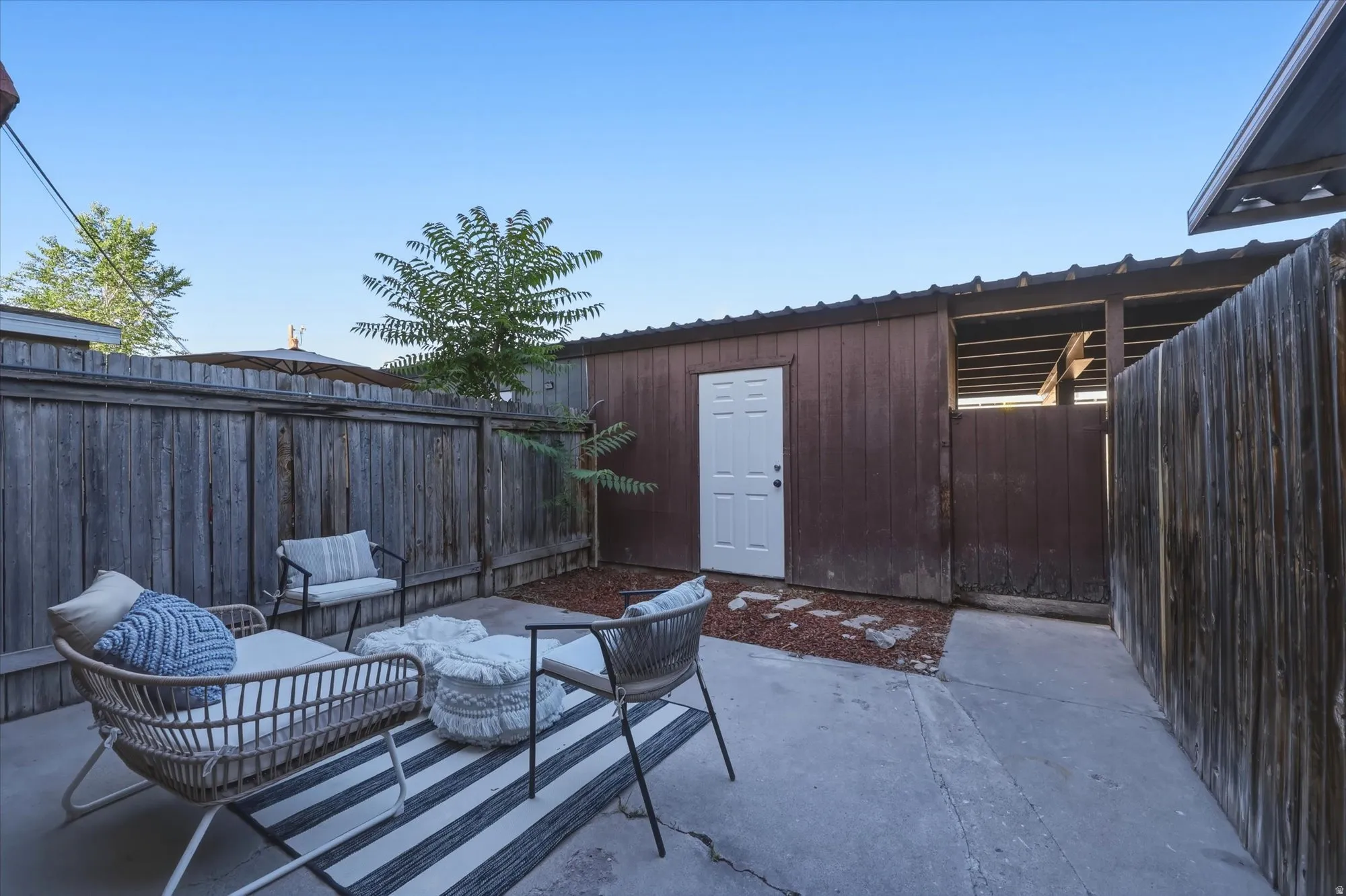 Private patio space featuring a concrete surface, perimeter fencing, and a detached storage shed with a white door