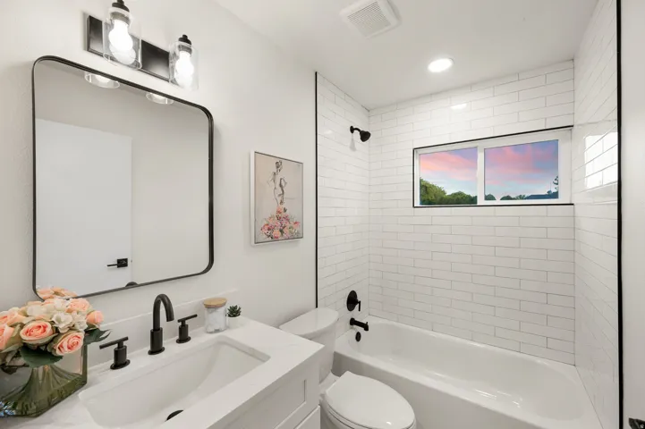 Modern bathroom featuring a white subway tile tub surround, white vanity with quartz-finish countertop, and matte black plumbing fixtures