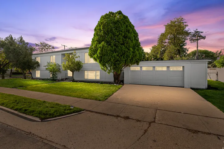 Mid-century modern exterior with a flat roofline, an attached two-car garage, expansive driveway, and a concrete sidewalk