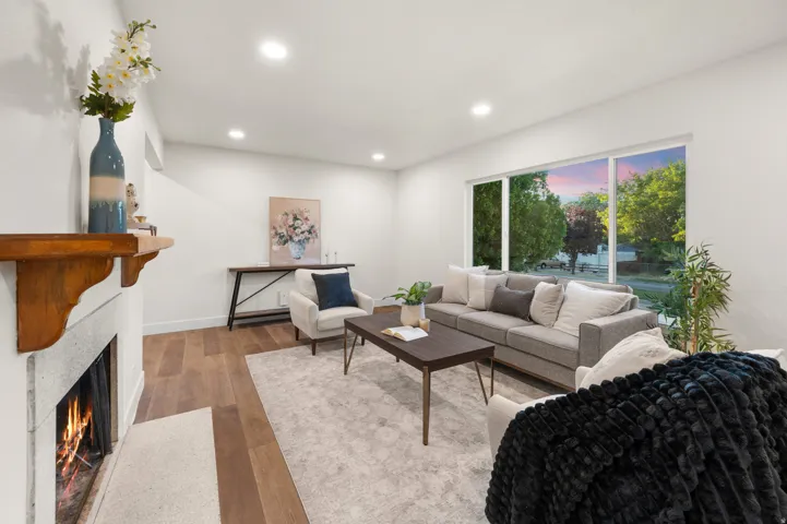 Living area featuring wood-finish flooring, a stone fireplace with a wood mantle, a large picture window, and recessed lighting
