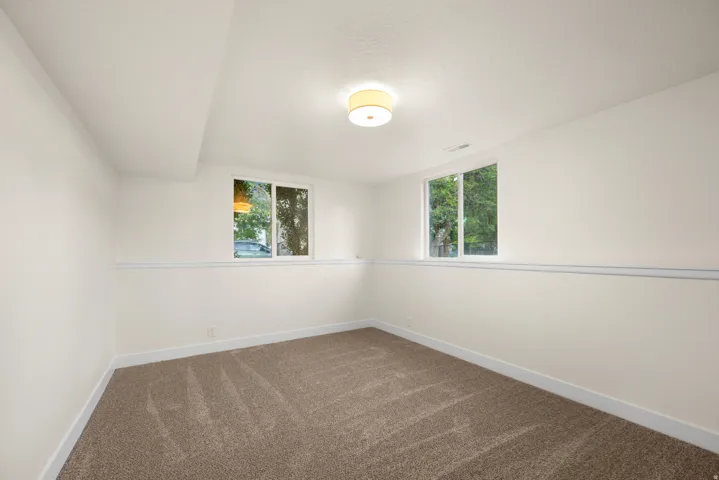 Finished room featuring neutral carpeting, white walls with chair rail molding, and two windows providing natural light
