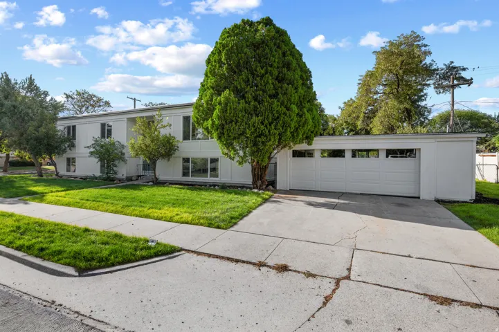 White exterior with multiple windows, attached garage with multiple garage doors, concrete driveway, and a manicured lawn