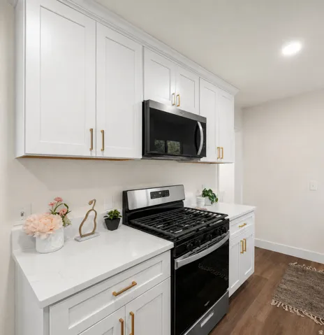 White shaker cabinetry, gold-finish hardware, stainless steel gas range, built-in microwave, wood-finish flooring