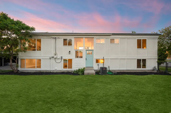 Modernist exterior featuring multiple large windows, a two-story entrance with transom windows, a light blue front door, and a manicured lawn