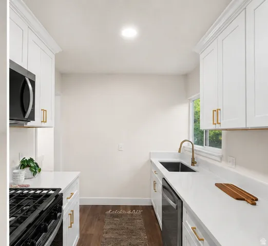 Galley kitchen featuring white cabinetry, gold-tone hardware, wood-finish flooring, white countertops, and a stainless steel sink with a gold-tone faucet
