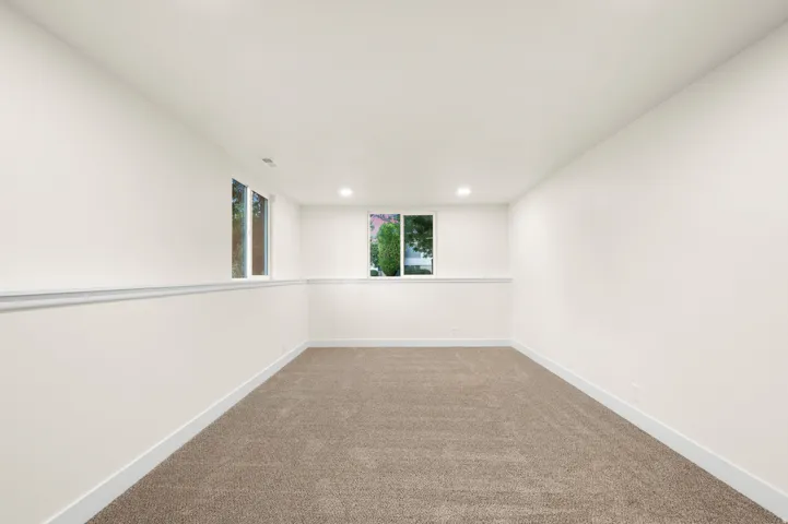 Spacious room featuring neutral carpeting, white painted walls, white trim, recessed lighting, and dual windows