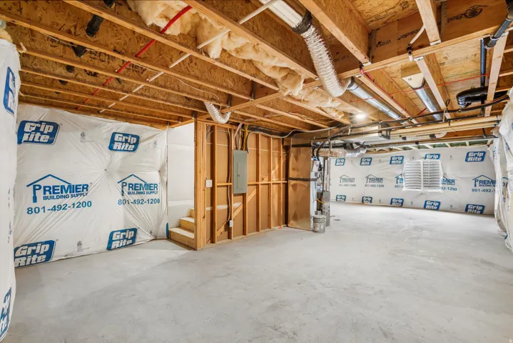 Unfinished basement space featuring exposed wood joists, concrete flooring, foundational walls with insulation, visible utility conduits, and a wood-framed stair structure