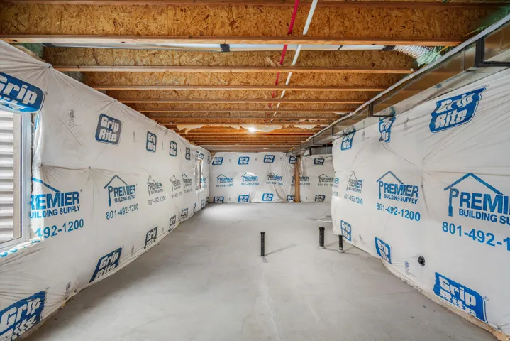 Unfinished basement area featuring exposed wooden joists, concrete flooring, exterior wall insulation, and visible plumbing rough-ins