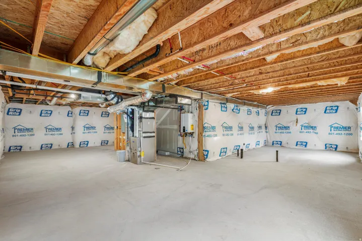 Unfinished basement with exposed wood joists and subflooring, concrete slab flooring, and perimeter walls insulated with white vapor barrier