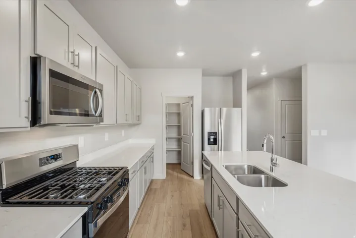 **DISCLAIMER** Interior package may vary. Modern kitchen featuring light gray cabinetry, stainless steel appliances, white countertops, a central island with double basin sink, and wood-finish flooring