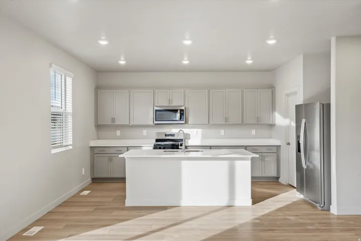 **DISCLAIMER** Interior package may vary. Kitchen featuring an integrated island with a stainless steel sink, light grey cabinetry, stainless steel appliances, white countertops, and wood-finish flooring