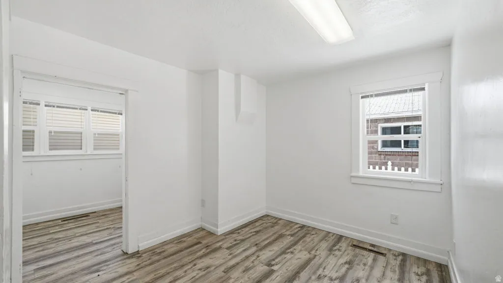 Bright room featuring wood-finish flooring, white walls, and a rectangular window with white blinds