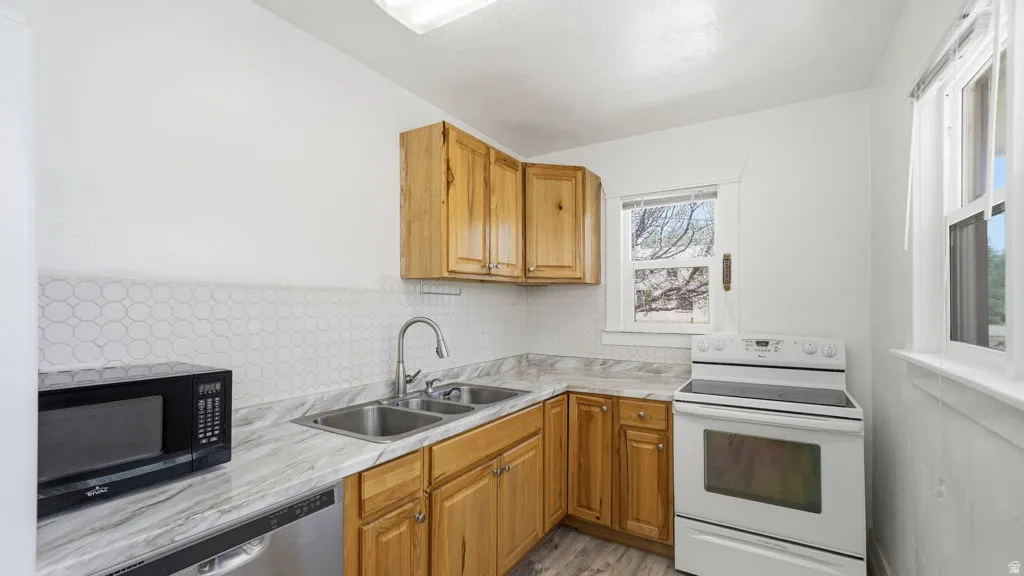 Kitchen featuring natural wood-finish cabinetry, a dual basin sink, white patterned backsplash, and a white electric range