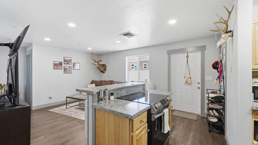 Open-concept living space featuring wood-finish flooring, recessed lighting, a kitchen island with granite-style countertops, and a built-in electric range