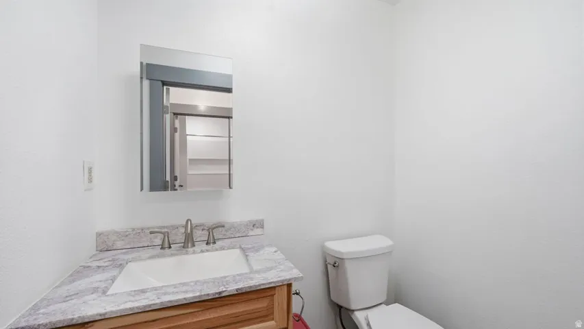 Powder room featuring a wood-finish vanity with an integrated sink, a light-toned countertop, and a wall-mounted mirror