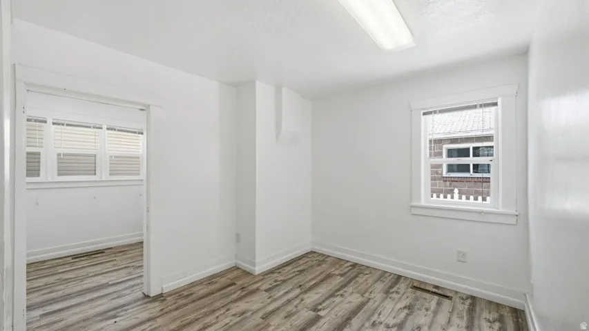 Bright room featuring wood-finish flooring, white walls, and a rectangular window with white blinds