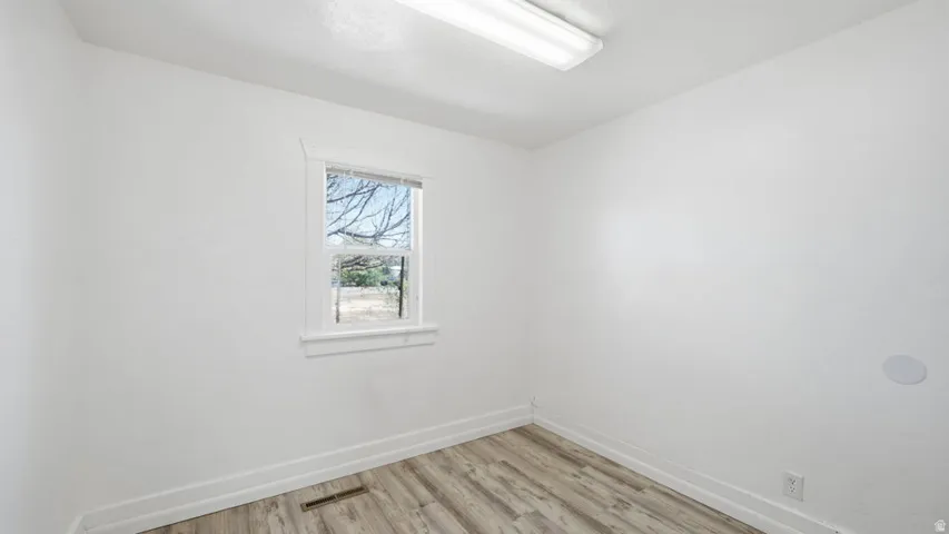 Interior space featuring a single window with white trim, wood-finish flooring, white walls, and a ceiling-mounted fluorescent light fixture
