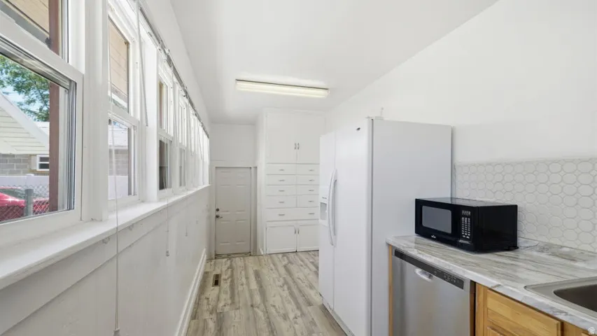Elongated room featuring a continuous wall of multiple windows, wood-finish flooring, built-in cabinetry, a white refrigerator, and a light-toned countertop with a geometric tile backsplash