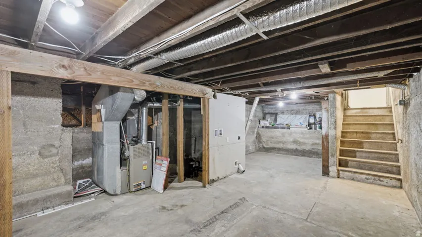 Unfinished basement featuring concrete flooring, exposed wood beam ceiling, concrete block walls, and a visible furnace unit