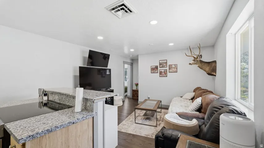 Open-concept living area featuring a kitchen peninsula with a cooktop, granite-style countertops, wood-finish flooring, and recessed lighting