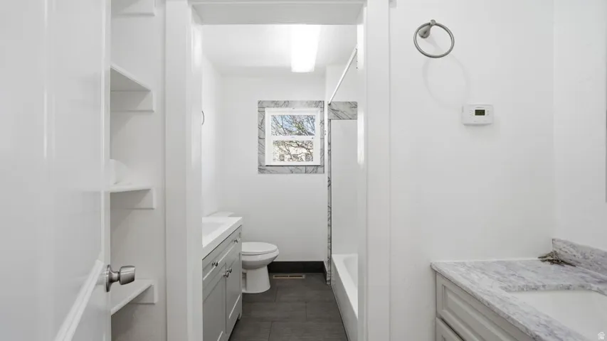 Bathroom featuring a white bathtub, toilet, and gray tiled flooring