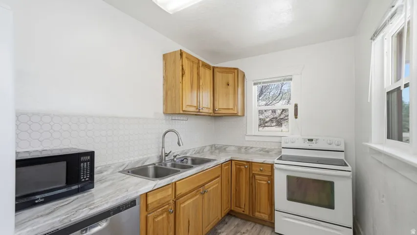 Kitchen featuring natural wood-finish cabinetry, a dual basin sink, white patterned backsplash, and a white electric range