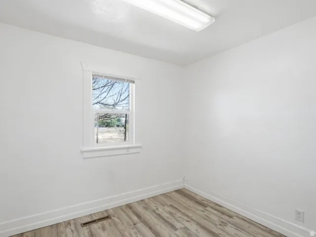 Interior space featuring a single window with white trim, wood-finish flooring, white walls, and a ceiling-mounted fluorescent light fixture