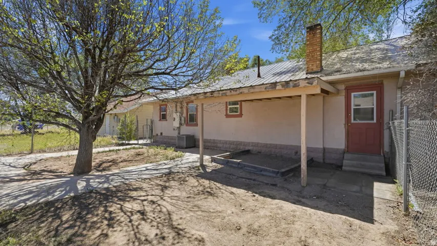Rear exterior featuring a covered patio with exposed wood supports, a corrugated metal roof, and a brick chimney