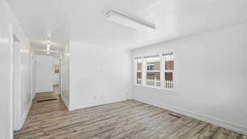 Spacious room featuring wood-finish flooring, white walls, and a large window with white trim