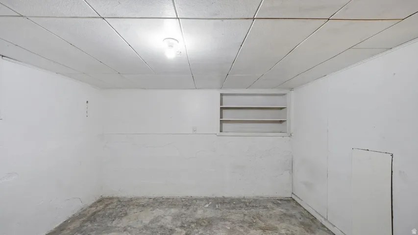 Unfinished room featuring white painted walls, a drop ceiling with recessed lighting, built-in shelving, and a concrete floor