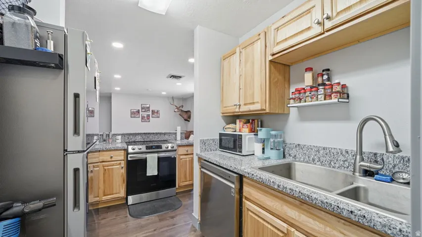 Kitchen featuring wood-finish cabinetry, granite-style countertops, and stainless steel appliances including a refrigerator, range, and dishwasher