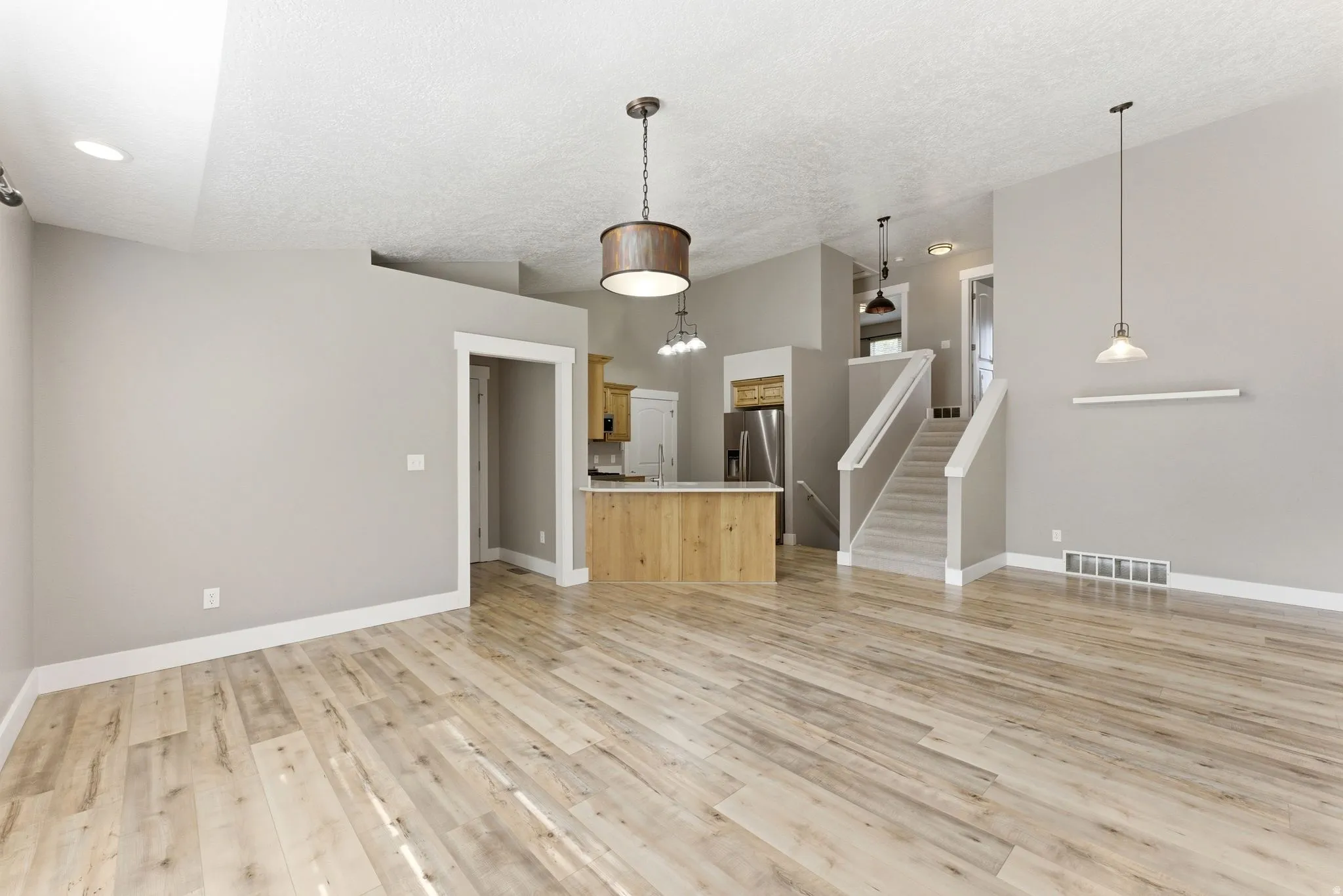 Open-concept interior featuring new LVP flooring, a kitchen island with a wood-finish base, stainless steel appliances, and a carpeted staircase