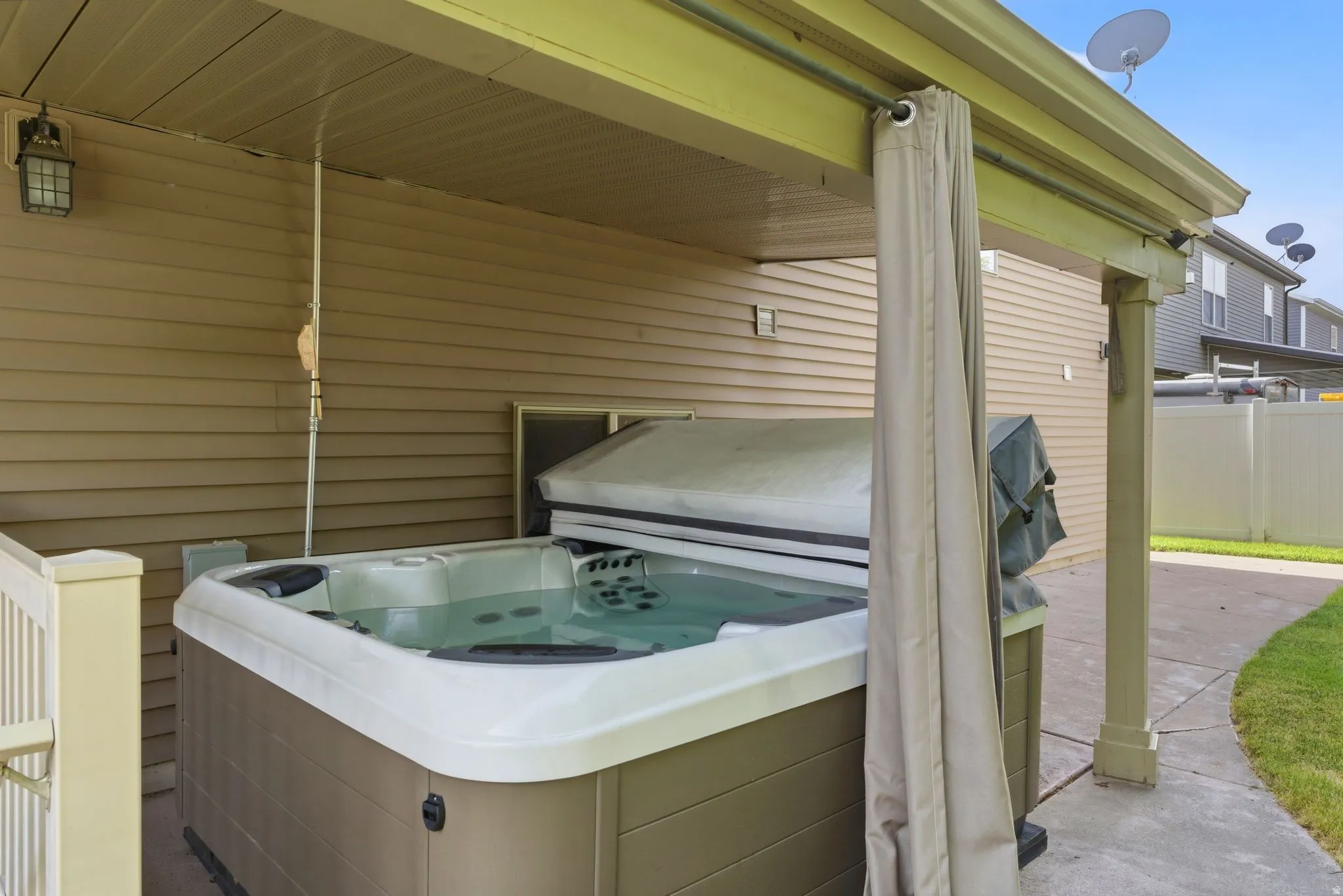 Covered patio area featuring a built-in hot tub, privacy curtain, exterior light fixture, and concrete patio flooring