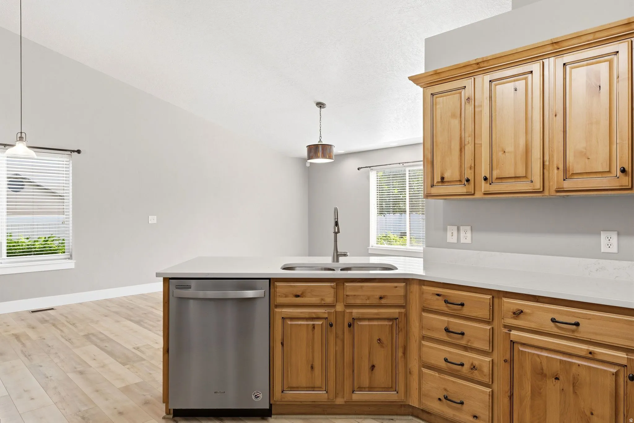 Kitchen featuring wood cabinetry, stainless steel dishwasher, double basin sink with high-arc faucet, and light-toned countertops