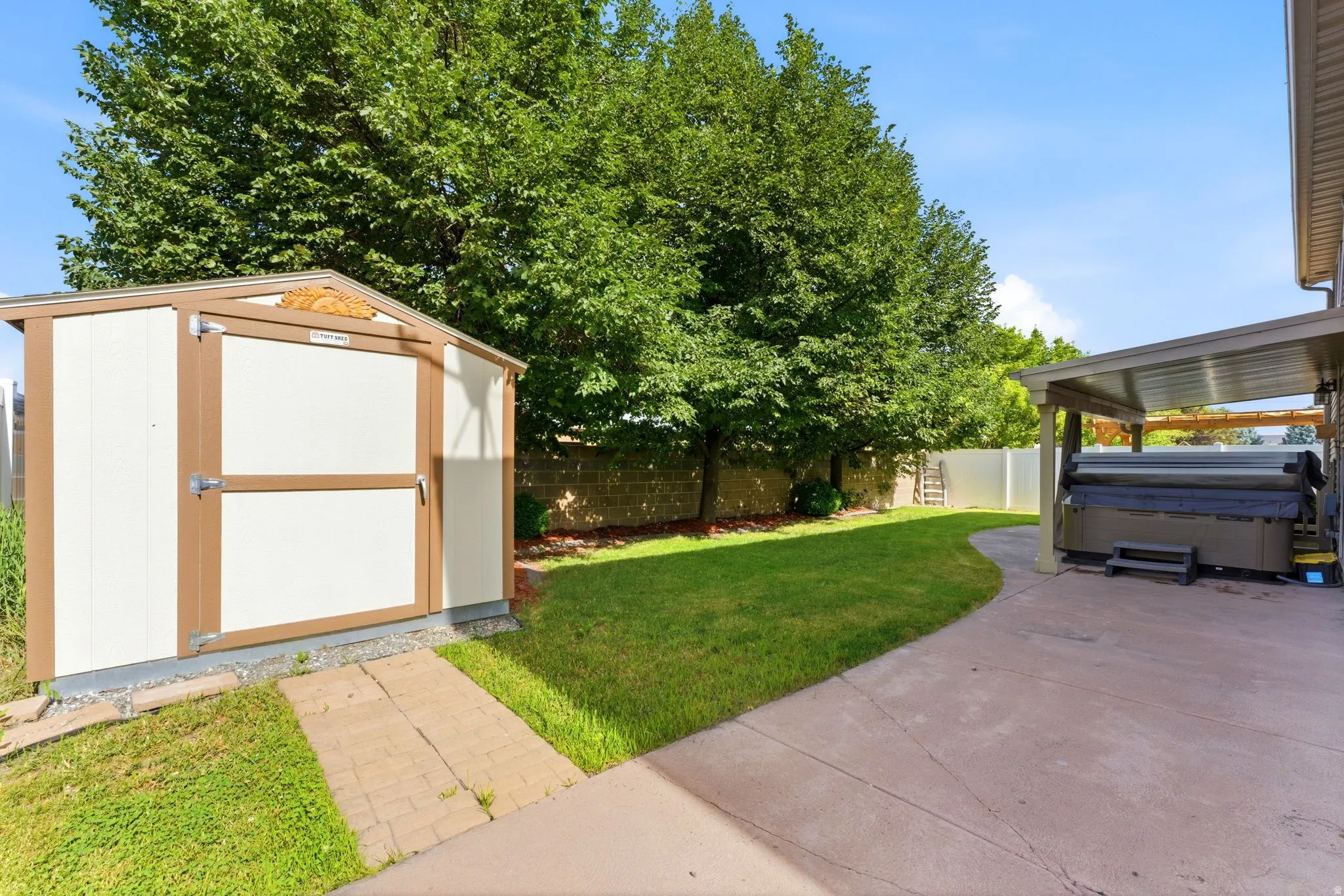 Manicured lawn with mature trees, a detached storage shed, and a covered patio area with an integrated hot tub