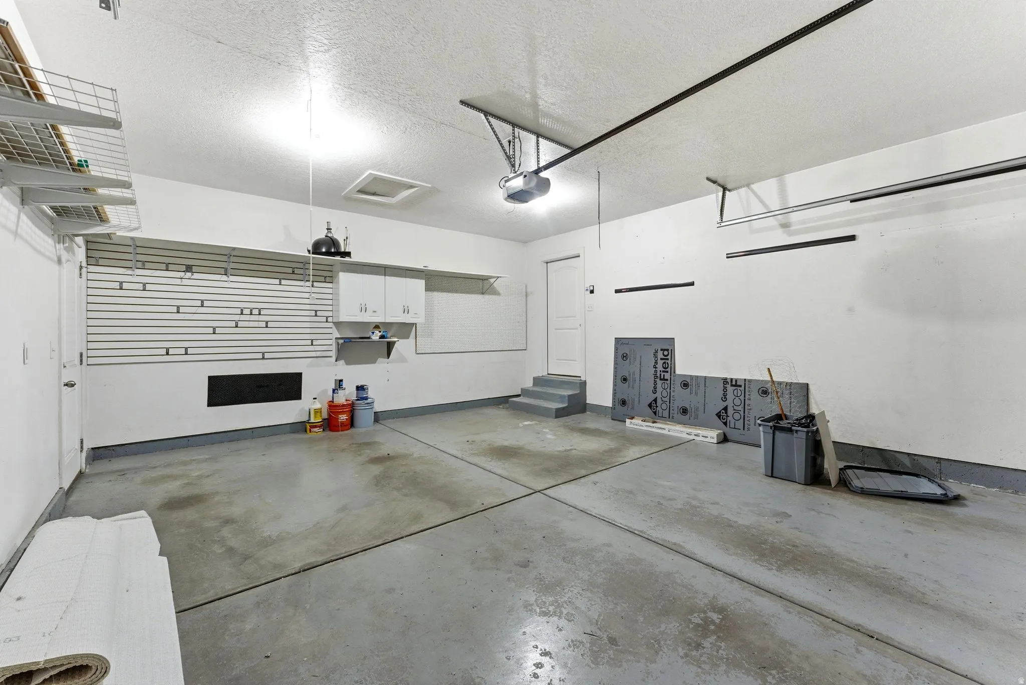 Spacious garage featuring a concrete floor, built-in wall shelving, integrated cabinetry, overhead lighting, and an automatic garage door opener