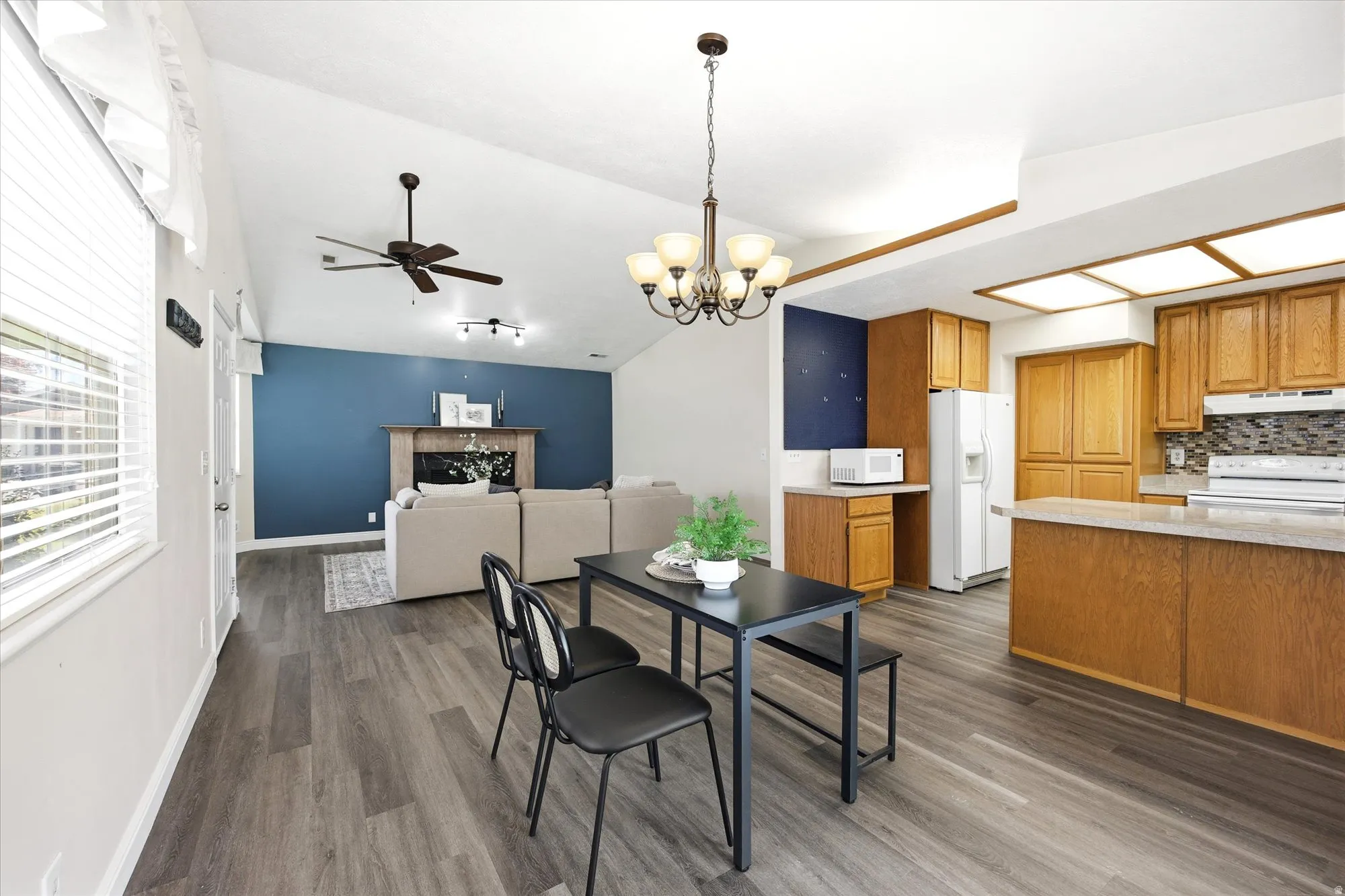 Open-concept living space featuring wood-finish flooring, vaulted ceilings, and a central chandelier